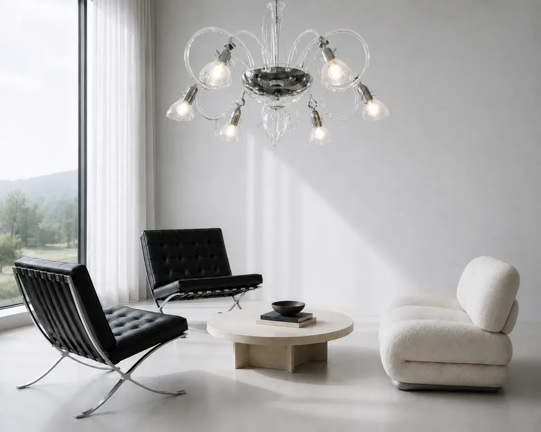 Kronleuchter aus klarem Glas mit geschwungenen Armen über zwei schwarzen Ledersesseln, einem runden hellen Tisch und einem weißen Sofa
