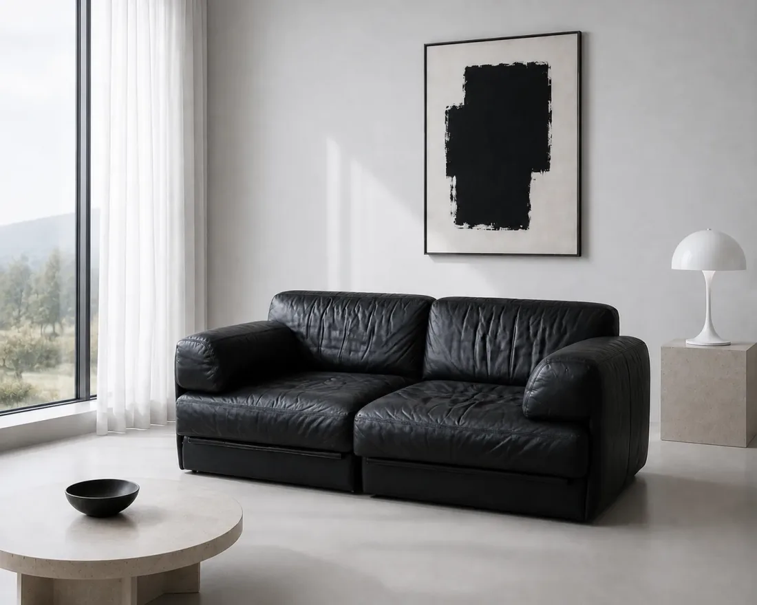 Schwarzes Ledersofa vor heller Wand mit Tischleuchte und Beistelltisch